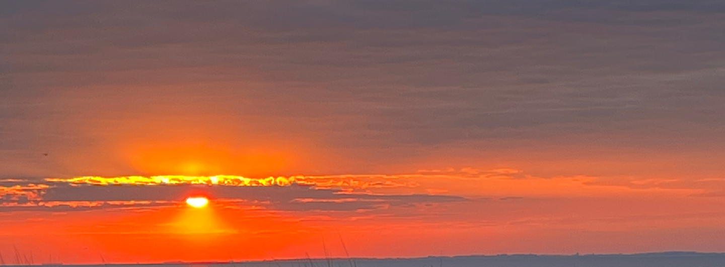 Vor grauviolettem Himmel im oberen Drittel geht die Sonne leuchtend hinter einem orangeroten Wolkenband unter. von K. Schwahlen lizensiert unter CC BY-SA